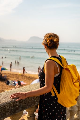 A vertical shot of a young Caucasian female in a hat looking at the sea on the beach