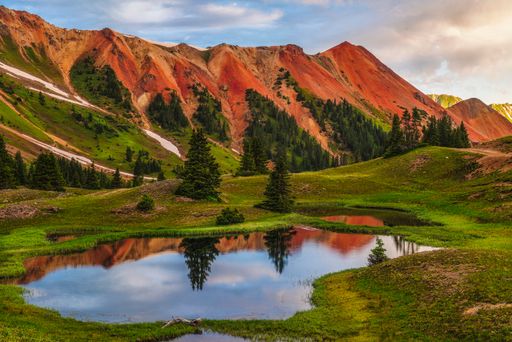 Scenic pond in lush field with mountains and cloudy sky