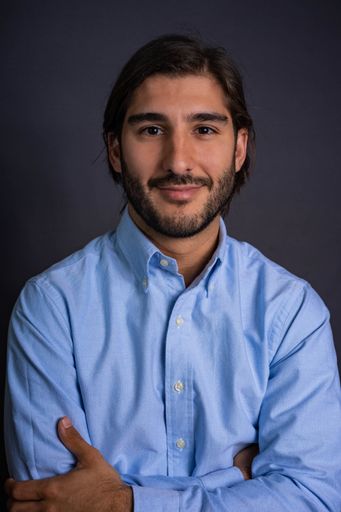 Studio Portrait of Hispanic Man with Beard and Long Hair in Blue Shirt Looking at Camera with Confident and Friendly Gesture Crossing Arms