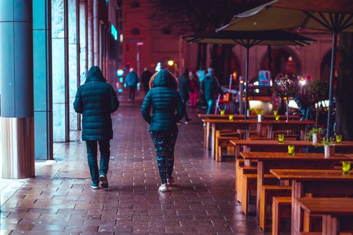 Couple of female friends walking in rainy night in urban setting near Munich Isartor besides a bar.