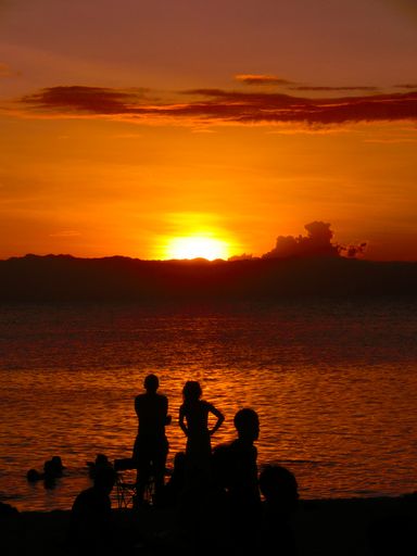 A vertical shot of a silhouette of a group of people relaxing on a sandy beach by the sea