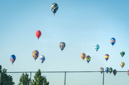 Numerous hot air balloons soar above a tennis court in Iowa