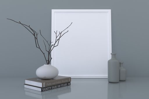 A frame with a blank canvas, books, decorative branches in a vase, and ceramic bottles