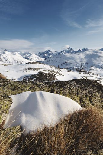 A panoramic shot of snow covered French alps with the sun shining under blue skies