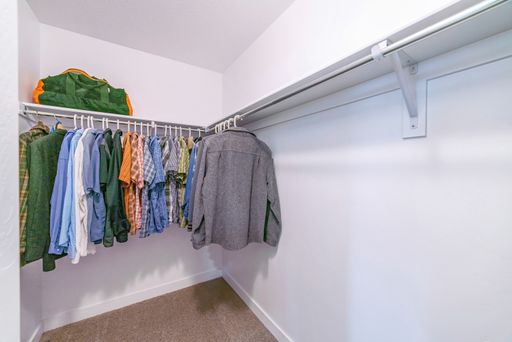 Many clothes in a wardrobe room with white wooden shelves and racks