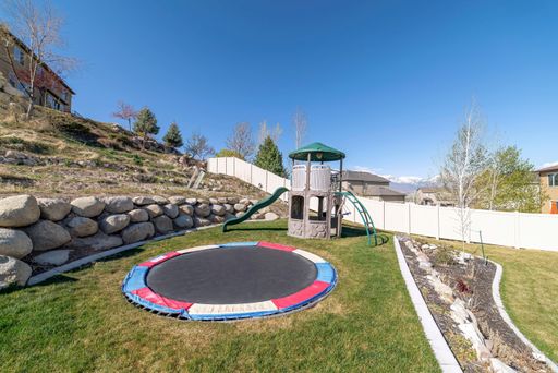 a trampoline and a slide in a green fenced area