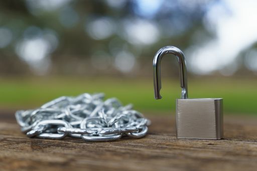close-up of an open padlock next to a chain strung on a wooden table in a field with an out-of-focus background