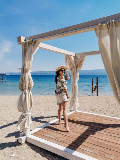 Beautiful young woman wearing beach coverup and sun hat standing on wooden deck on sandy beach in summer.