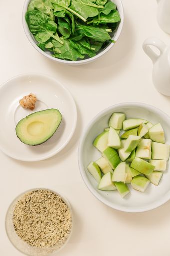 A top view of avocados, greens, and apples on a white table