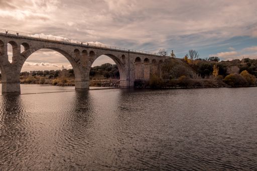 A beautiful shot of an arch bridge with scenery of sunset and a cloudy sky in the background