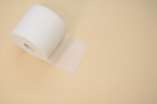 a top view of a sterile gauze bandage roll isolated on a light beige background on the left side