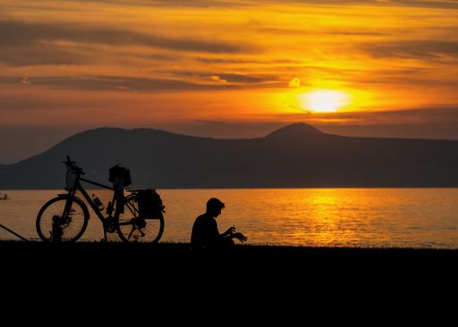 A person gazes at the sunset over the water with their bicycle beside them.