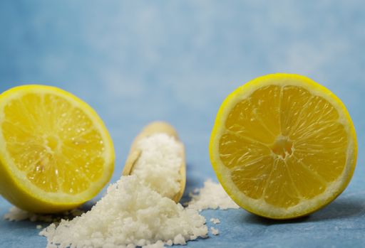 lemon cut in half with salt on a wooden spoon on a blue background and copy space