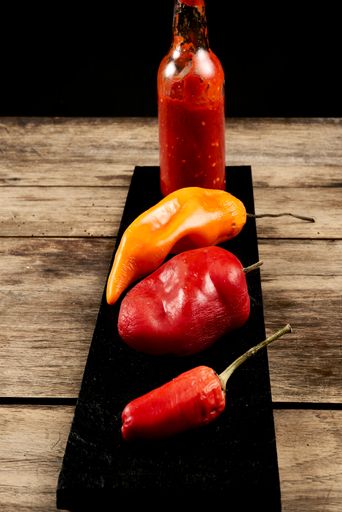 A vertical shot of yellow and red bell peppers with chili sauce on a black pla
