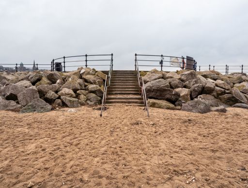 Stone steps up off the empty sandy beach up the sea wall onto the promenade quite winters day.