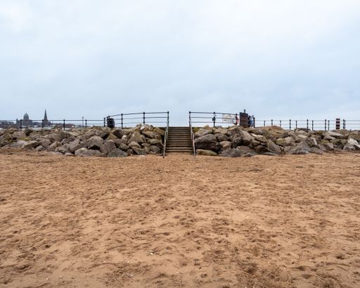 Stone steps up off the empty sandy beach up the sea wall onto the promenade quite winters day.