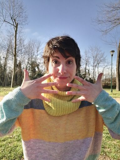 A vertical shot of a cool Caucasian woman with colorful cloth showing fingers in a park