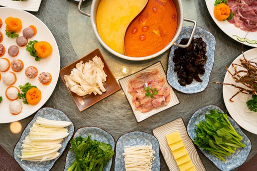 A high angle shot of soup near a plate with raw meat with a side dishes