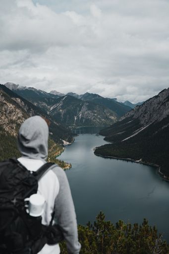 Male person with hoodie and backpack standing infront of Plansee in Austria
