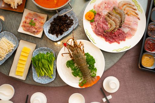 A high angle shot of a lobster near a plate with raw meat and side dishes on a round table