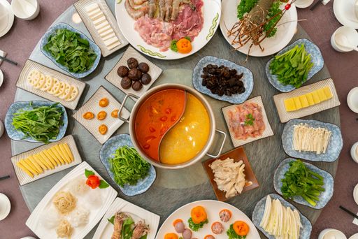 A  big round table with different side dishes on it with soup in the middle