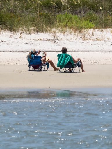 A couple sitting in a beach chair on grassy shore