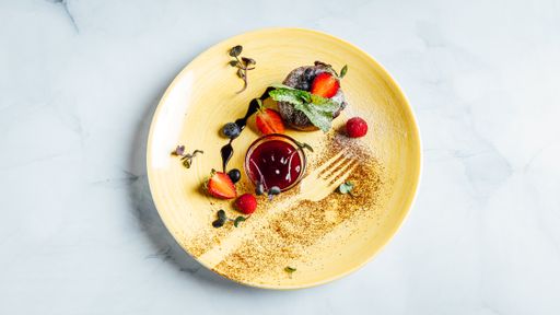 A top view of a chocolate muffin with a  bowl of strawberry jam on the plate