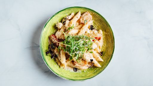 A top view of a fresh delicious penne pasta with shredded cheese and arugula on the plate