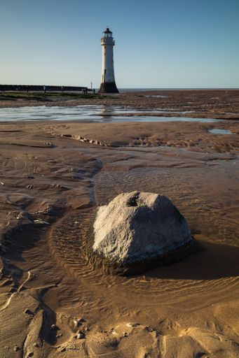 A vertical shot of a rock in the small sandy pond with the lighthouse in the background