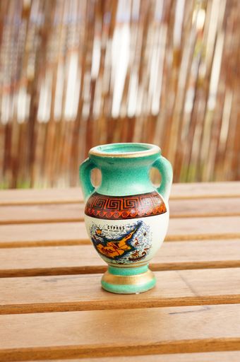 A vertical closeup shot of a Greek vase on a wooden table with a blurry background