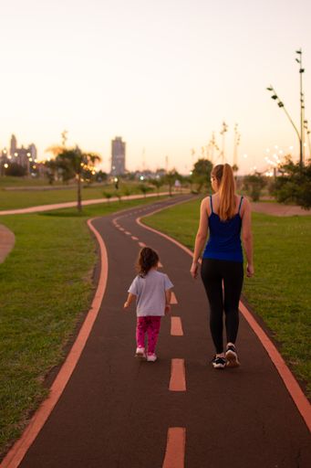A vertical back view of a young Hispanic fit female and her daughter on a running track