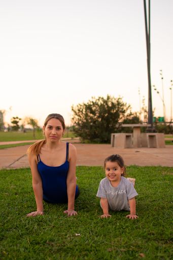 A vertical shot of a young Hispanic fit female and her daughter exercising and posing on the grass