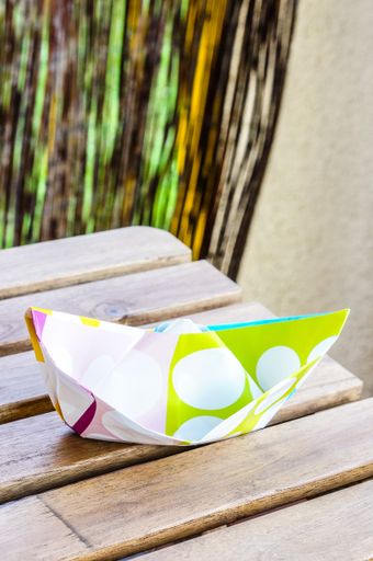 A vertical closeup shot of a colorful handmade paper boat on a wooden table