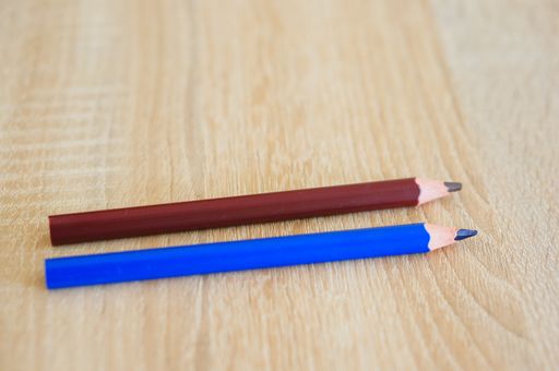A closeup shot of two blue and brown drawing pencils on a wooden surface
