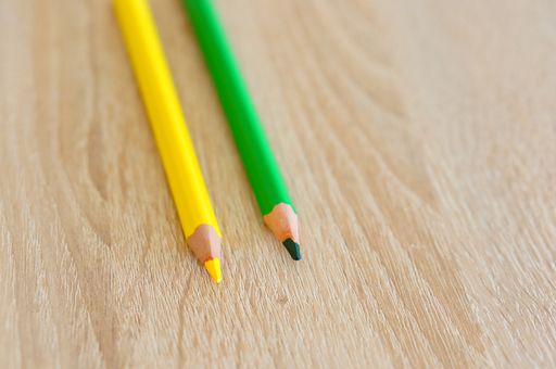 A closeup shot of two yellow and green drawing pencils on a wooden surface