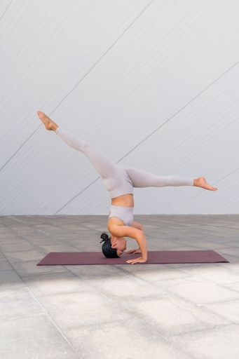 A brunette woman dressed in sportswear performing salamba sirsasana 2 yoga posture with legs open.