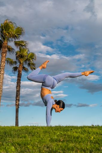 A brunette woman doing a handstand or yoga posture adho mukha vrksasana with legs forward in the park.