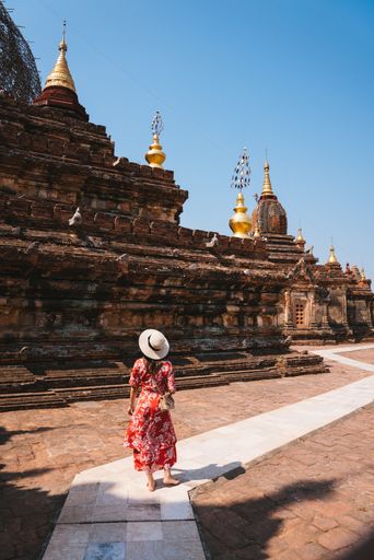 A vertical shot of a female with a red dress walking near a temple on a sunny day at Myanmar, Began