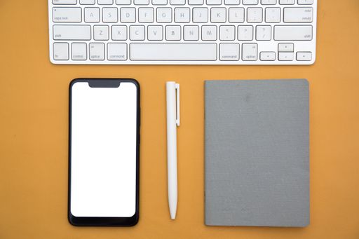 A top view of a keyboard, smartphone, notebook and a pen