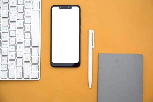 A top view of a keyboard, smartphone, pen and a notebook