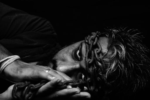 A grayscale portrait of an angry looking man with chained head and hands