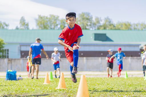 A young football player performs warm-up exercises. Snake running among the guide cones. Preparing for future victories. Outdoor training.