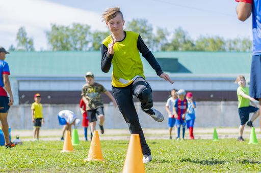 A young football goalkeeper performs warm-up exercises. Snake running among the guide cones. Preparing for future victories. Outdoor training.