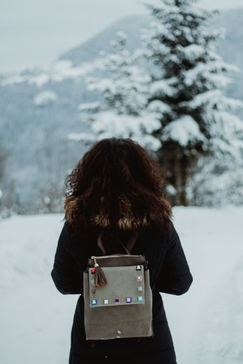 A vertical back view of a female with a backpack on a snowy field