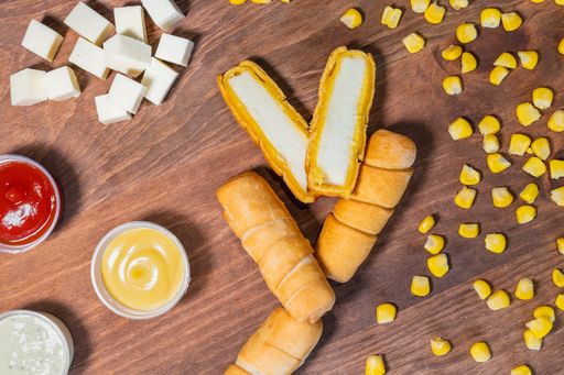 Venezuelan cheese tequenos cut in half on a wooden bottom with sauces garnished with cubes of cheese and shelled corn.