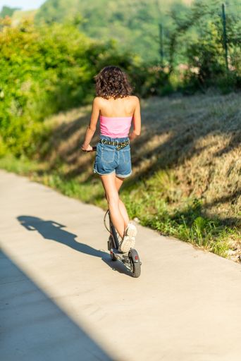 A vertical shot of a sexy woman riding an electric scooter on a summer day
