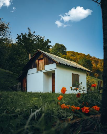 A vertical shot of a white gable-roofed house with a green yard on mountain slope