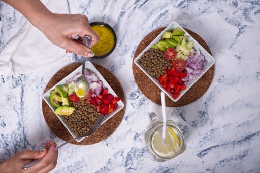 View from above of hands picking up the lentil salad with pieces of avocado, cherry tomato and onion with a fork and spoon.