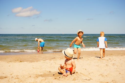 Children playing on sand close by the water on a sandy beach on a warm day.
