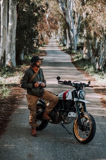 A motorcyclist stands beside their motorcycle on a clear day